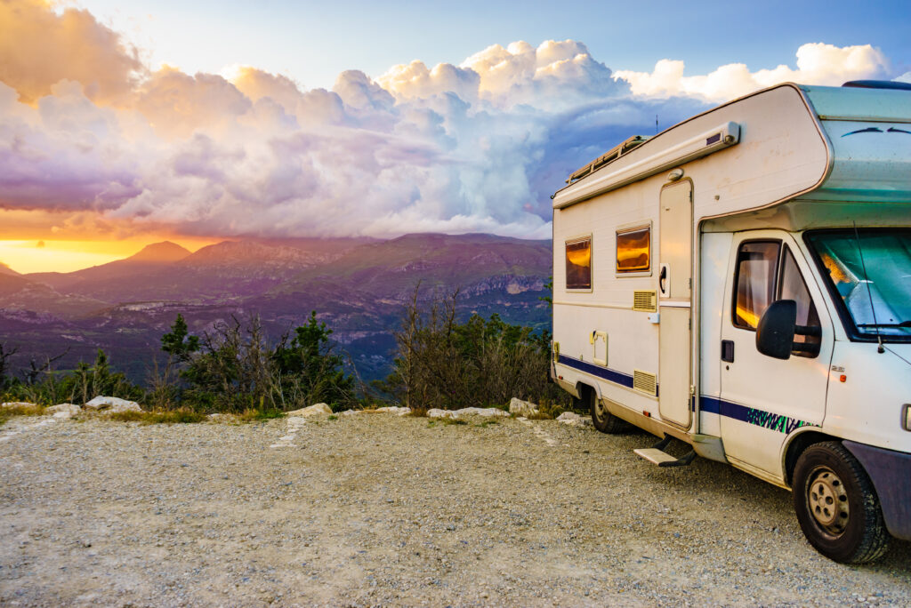A motorhome near a cliff with mountains in the background at sunset