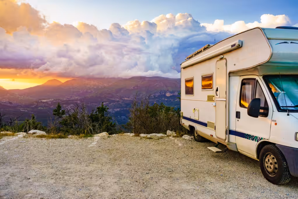 A motorhome near a cliff with mountains in the background at sunset