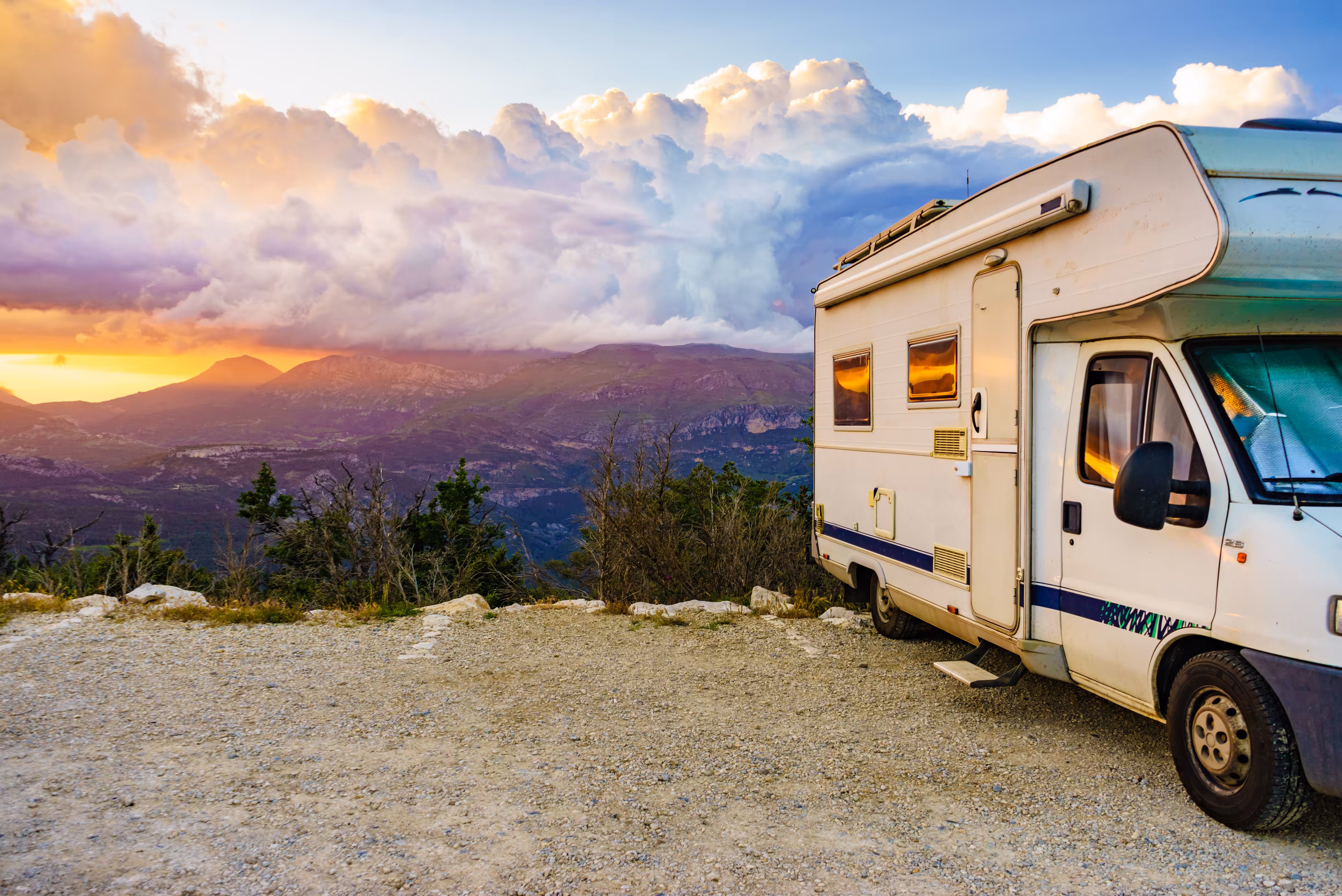 A motorhome near a cliff with mountains in the background at sunset